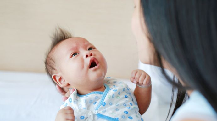 Ibu Mengalami Baby Blues - Seorang ibu baru yang terlihat cemas dan lelah, duduk di sofa dengan bayinya, menggambarkan perasaan emosional yang umum setelah melahirkan